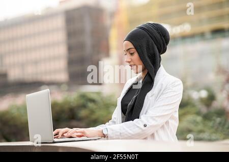 Beautiful Arab businesswoman wearing headscarf using laptop outdoors Stock Photo