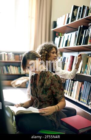 Female students reading books while sitting in library