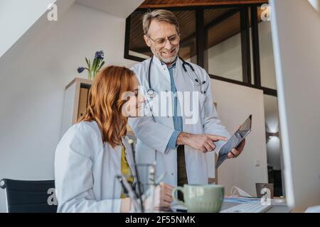 Male doctor showing digital tablet to coworker while standing at clinic Stock Photo