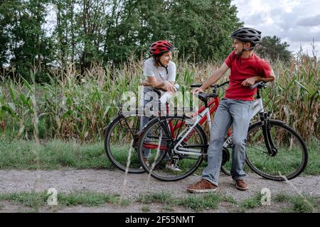 Father and daughter talking while leaning on bicycle at agricultural field Stock Photo