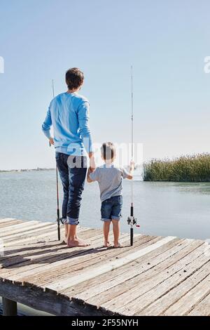 Father and son with fishing rods holding hands while standing on pier Stock Photo