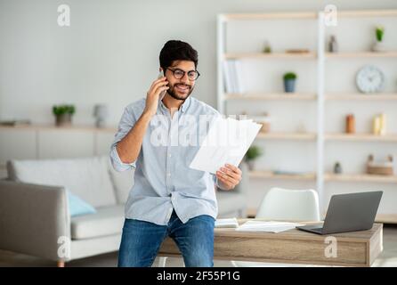 Home office. Confident arab entrepreneur talking with companion on phone and checking financial reports Stock Photo