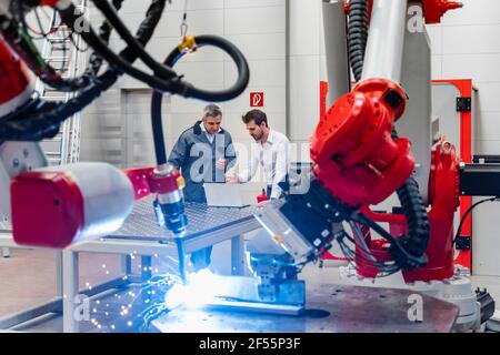 Robotic arm welding while male entrepreneurs working with laptop in factory Stock Photo