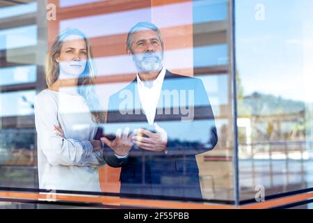 Confident professionals with digital tablet looking through window while standing at office Stock Photo