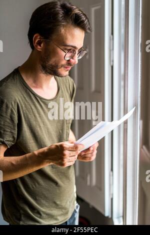 Young male entrepreneur looking at documents while standing near window in office Stock Photo