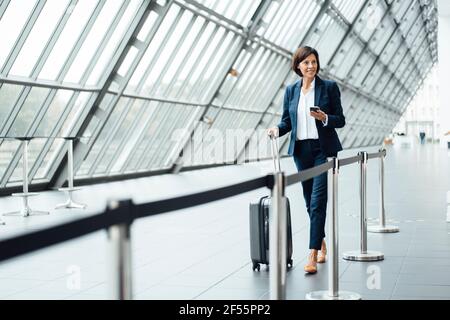 Mature businesswoman with suitcase walking in corridor Stock Photo