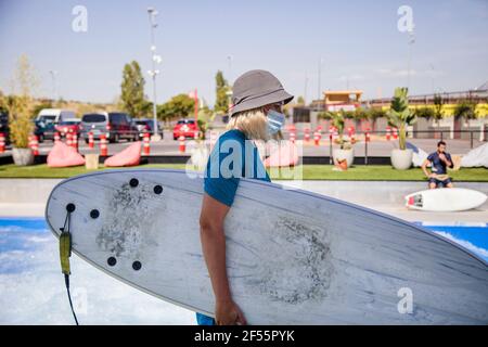 Female worker in bucket hat carrying surfboard while working during COVID-19 Stock Photo