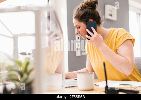 Female entrepreneur working while talking on smart phone Stock Photo