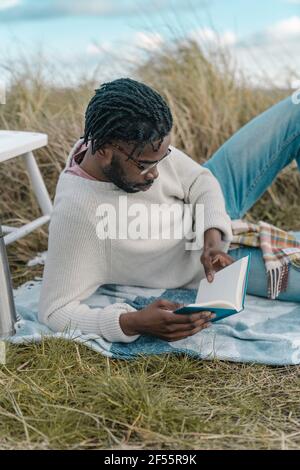Relaxed young man reading book while lying amidst dried plants Stock Photo