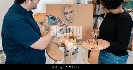 Young female painter learning from male artist at studio Stock Photo