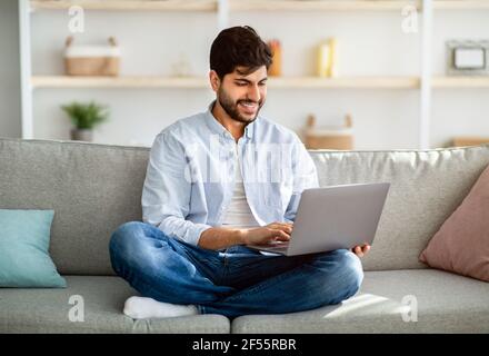 Remote work. Arab freelancer working on laptop computer at home, sitting on couch, enjoying distance job opportunities Stock Photo