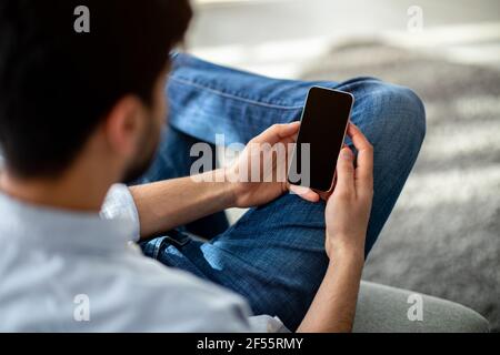 Over the shoulder view of unrecognizable man using cellphone with black empty screen for mockup Stock Photo