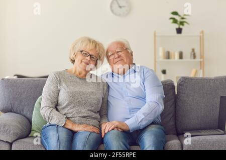 Smiling loving elderly couple wife and husband in jeans sitting on sofa and hugging Stock Photo