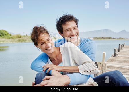 Happy couple sitting together on pier Stock Photo