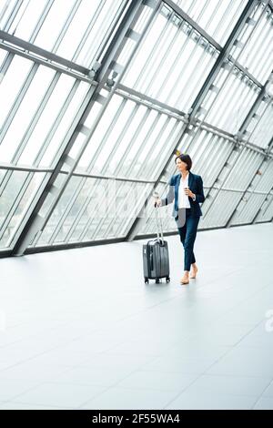 Female entrepreneur with suitcase looking away while walking in corridor Stock Photo