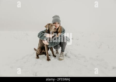 Portrait of teenage girl crouching in snow and embracing Labrador Retriever Stock Photo