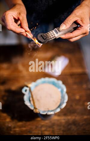Woman burning coal with matchstick over bowl of herbs Stock Photo