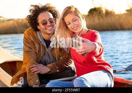 Smiling couple taking selfie through mobile phone while sitting in canoe on river Stock Photo