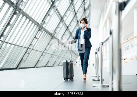 Female professional talking on smart phone while walking in corridor during pandemic Stock Photo