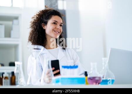 Smiling female scientist with smart phone looking away in hospital Stock Photo