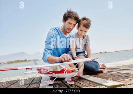 Mature man and boy talking while touching toy airplane on pier Stock Photo