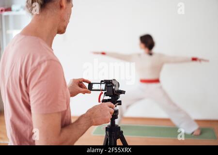 Man filming female instructor practicing yoga at health studio Stock Photo