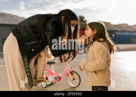 Mother wearing protective face mask cleaning face of daughter while standing on road Stock Photo