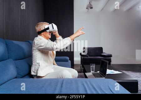 Senior businesswoman gesturing while using virtual reality headset on sofa Stock Photo