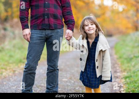 Cute girl smiling while holding father's hand standing in forest Stock Photo