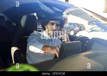 Businessman using GPS while talking on smart phone in car seen through windshield Stock Photo