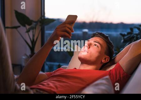 Relaxed young man lying on sofa while using smart phone in living room Stock Photo