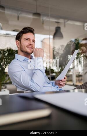 Thoughtful male entrepreneur with document looking away at office Stock Photo