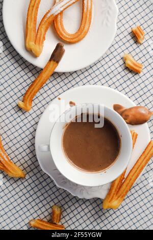 https://l450v.alamy.com/450v/2f55ygw/plate-of-churros-with-hand-of-man-pouring-hot-chocolate-in-background-2f55ygw.jpg