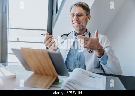 Smiling doctor discussing on video call over digital tablet while sitting at clinic Stock Photo