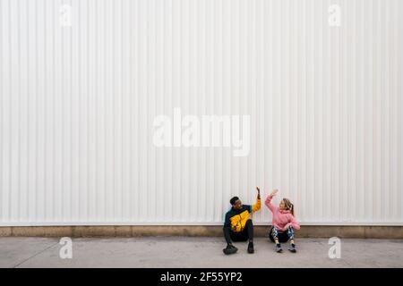 Man and woman doing high-five while sitting on floor against wall Stock Photo