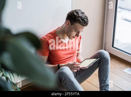 Young man using digital tablet while sitting against wall Stock Photo