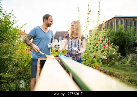 Smiling couple looking at each other while painting wooden planks in garden Stock Photo