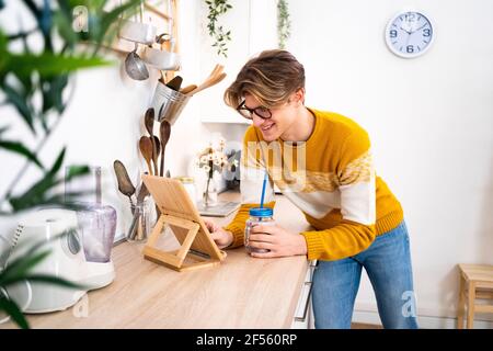 Young man using digital tablet while leaning on kitchen counter at home Stock Photo