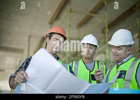 Male construction workers talking over plans at construction site Stock Photo