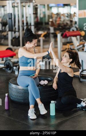 Happy female friends giving high-five while sitting in health club