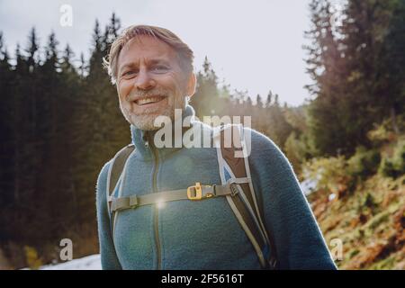 Smiling handsome man with backpack standing in forest against sky at Salzburger Land, Austria Stock Photo