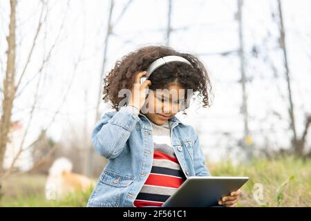 Boy listening through headphones while using digital tablet in nature Stock Photo