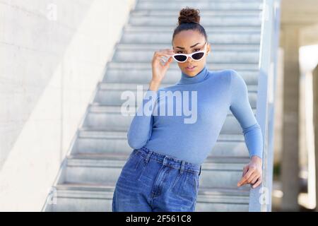 Woman staring through sunglasses while standing against staircase Stock Photo