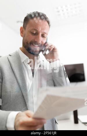 Smiling businessman holding documents talking on smart phone Stock Photo
