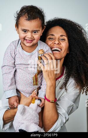 Cheerful mother carrying daughter against gray background Stock Photo