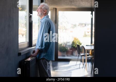 Smiling man looking through window while standing at home Stock Photo