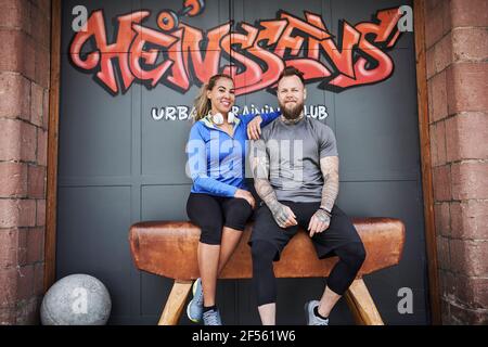 Female and male athletes sitting on bench outside gym against graffiti wall Stock Photo