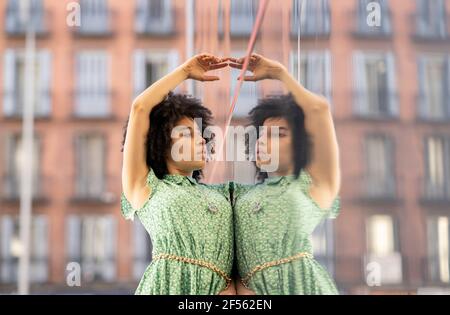 Young woman with hands raised while leaning against glass wall Stock Photo