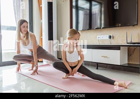 Young mother in sport clothing exercising at home with daughter. Online training during coronavirus covid-19 quarantine. Stay fit and safe during Stock Photo