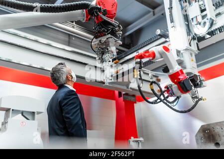 Mature automation engineer with protective face mask examining robotics in factory Stock Photo
